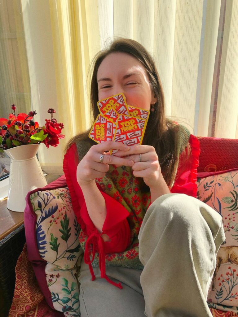 Rebecca, a white woman with long brown hair, is holding a bunch of cards to her face