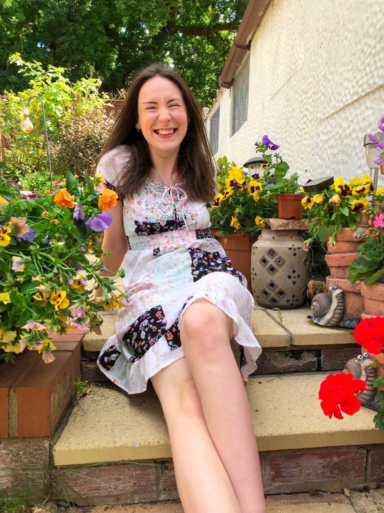 Rebecca, a white woman with brown hair is  sitting on a step in the garden. 